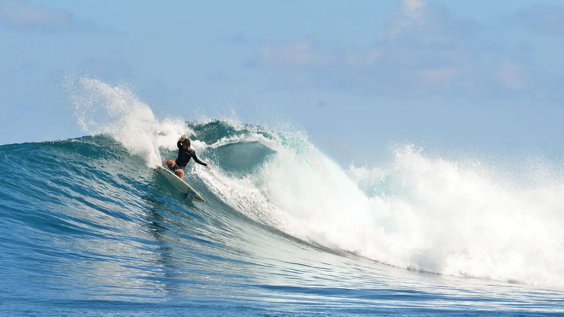 Surfer riding a right-hand point break on Ecuador's Pacific coast with lush green hills in the background
