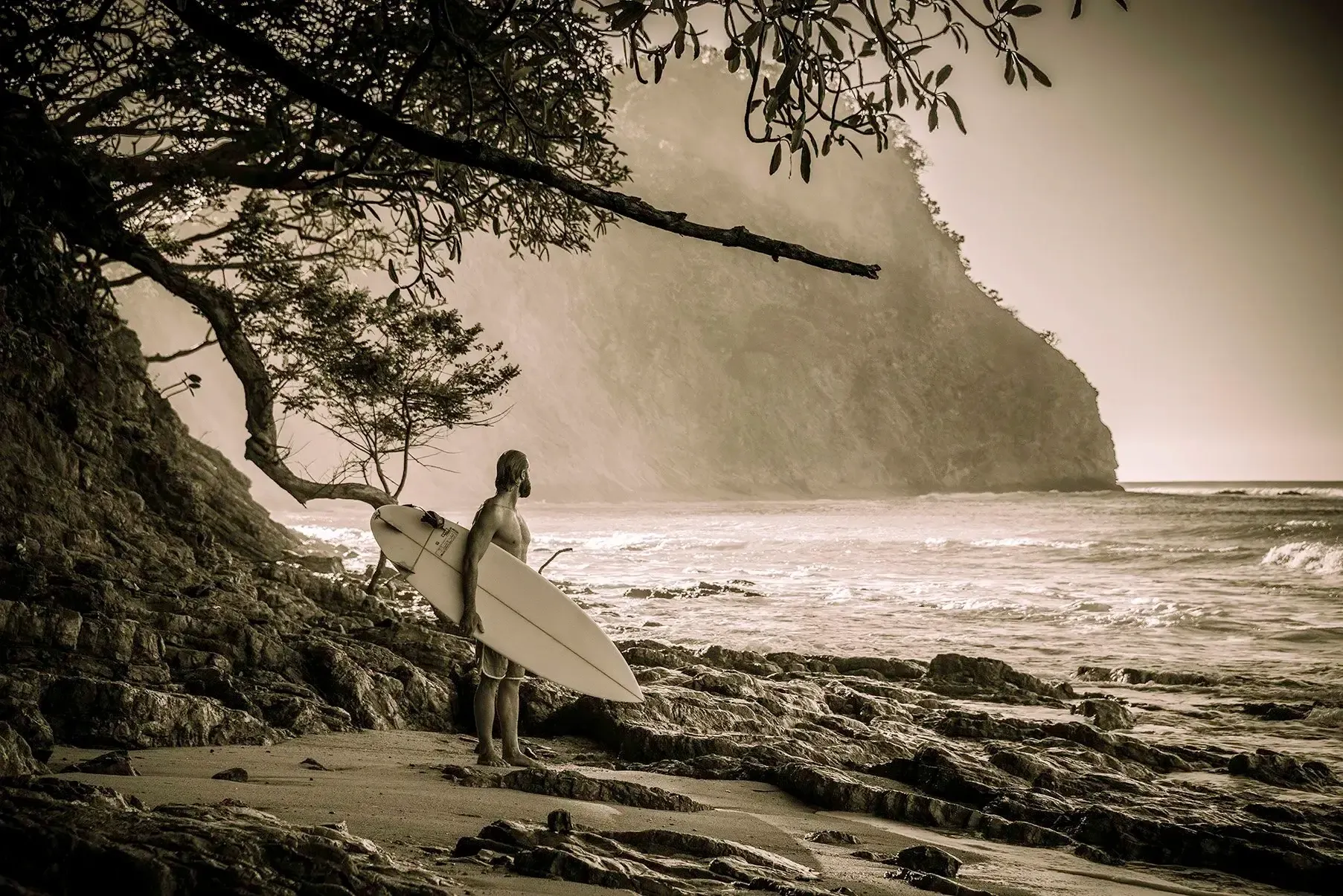 Jake Morrison, founder of Ecuador Surf Camp, standing on the beach at Montanita with a surfboard and the Pacific ocean behind him